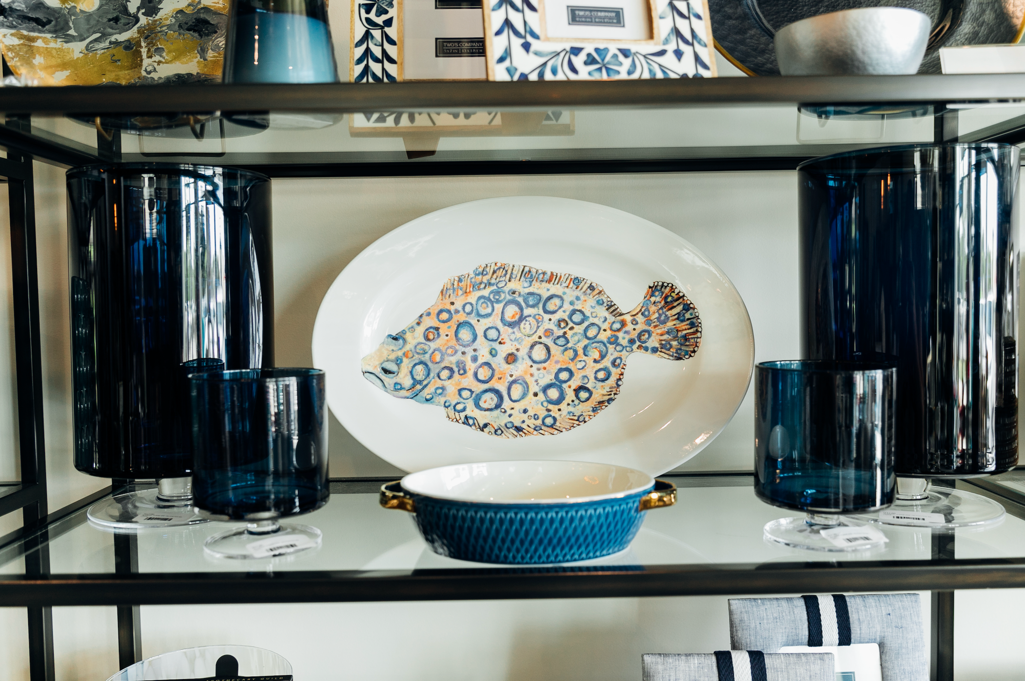 A platter with a fish painted on it next to dark blue hurricanes on a shelf